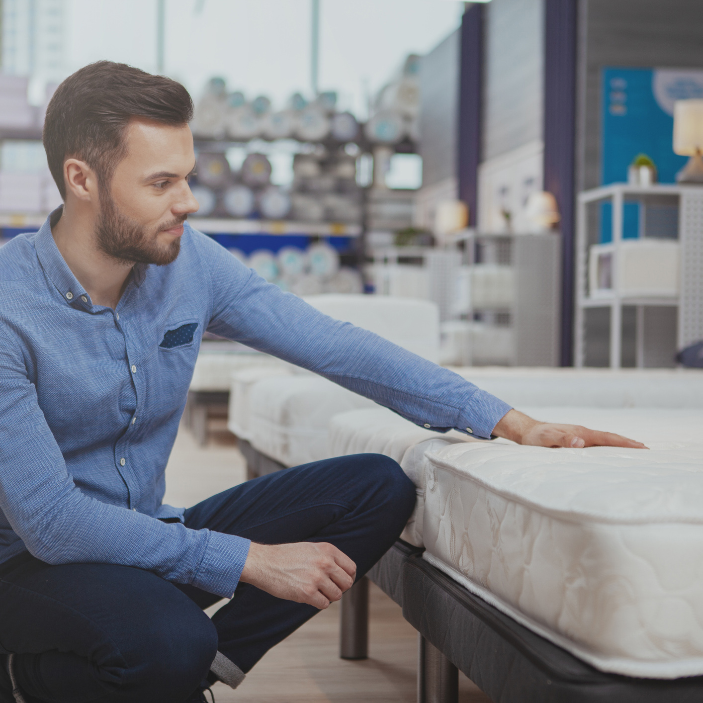 A man in a blue shirt goes mattress shopping